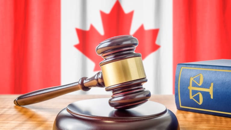 a gavel beside a lawbook and before the Canadian flag