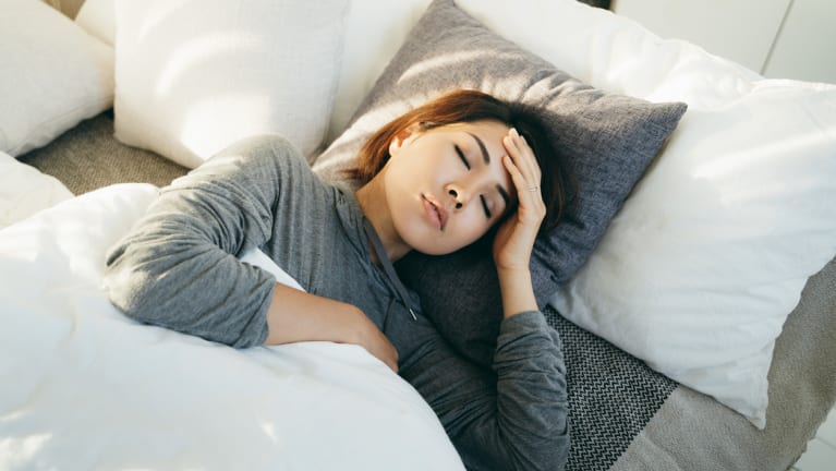 woman with hand on forehead lying in bed and feeling sick