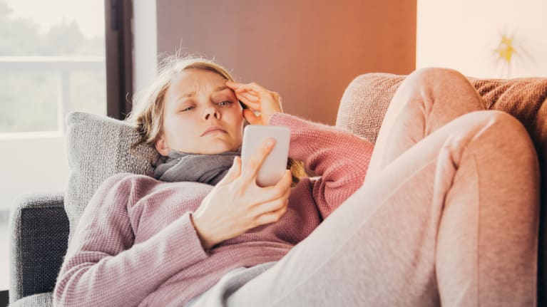 a woman on the couch with a hand to her head holding her cellphone in her other hand