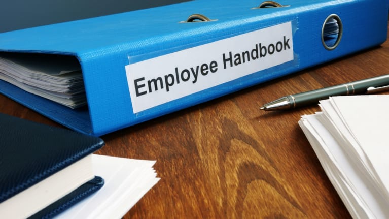 An employee handbook with two pens and a stack of paper