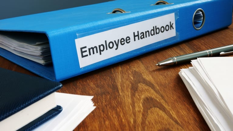 an employee handbook near two pens and a stack of papers