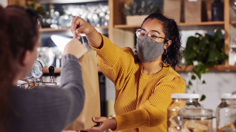 cafe worker wearing a amsk handing customer a bag