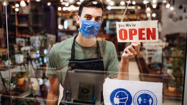 server wearing face mask and holding Open sign in cafe