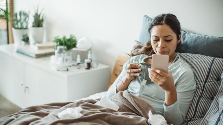 woman sick in bed with tea and smart phone