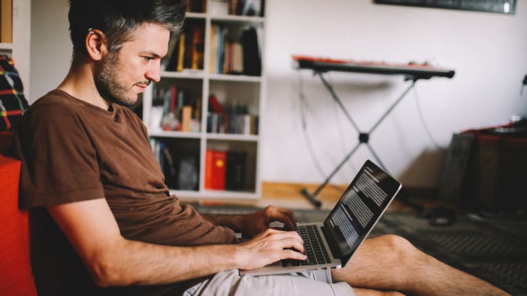 a telecommuting man in a T shirt and shorts working on his laptop