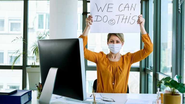 Businesswoman wearing mask and holding sign that reads: &quot;We can do this.&quot;