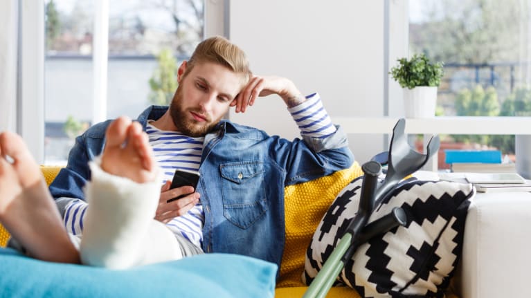 man with broken leg using smart phone at home
