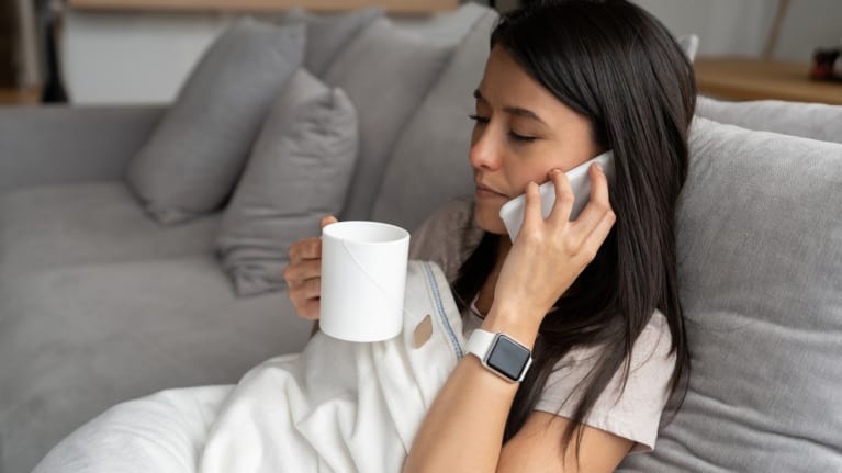 Woman feeling sick at home drinking tea and talking on phone