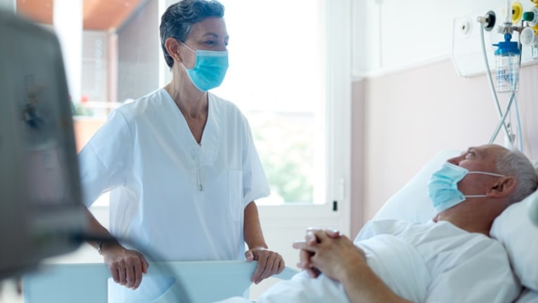 Doctor attending a patient in hospital bed, both wearing masks.