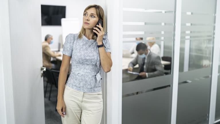 Worried-loooking woman on phone at work, surrounded by employees wearing masks.