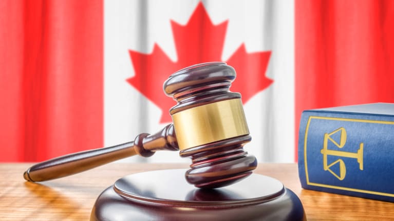 a gavel and law book in the foreground with the Canadian flag in the background