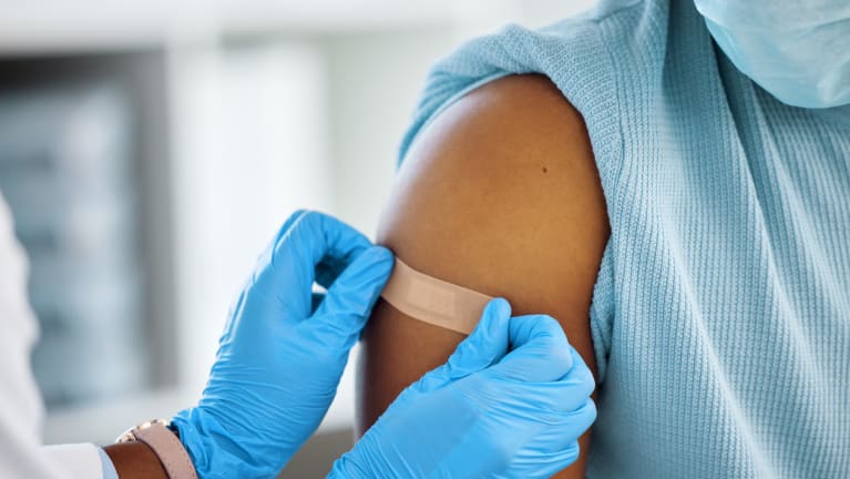 a medical professional applying a Band-Aid to  a patient&#39;s upper forearm